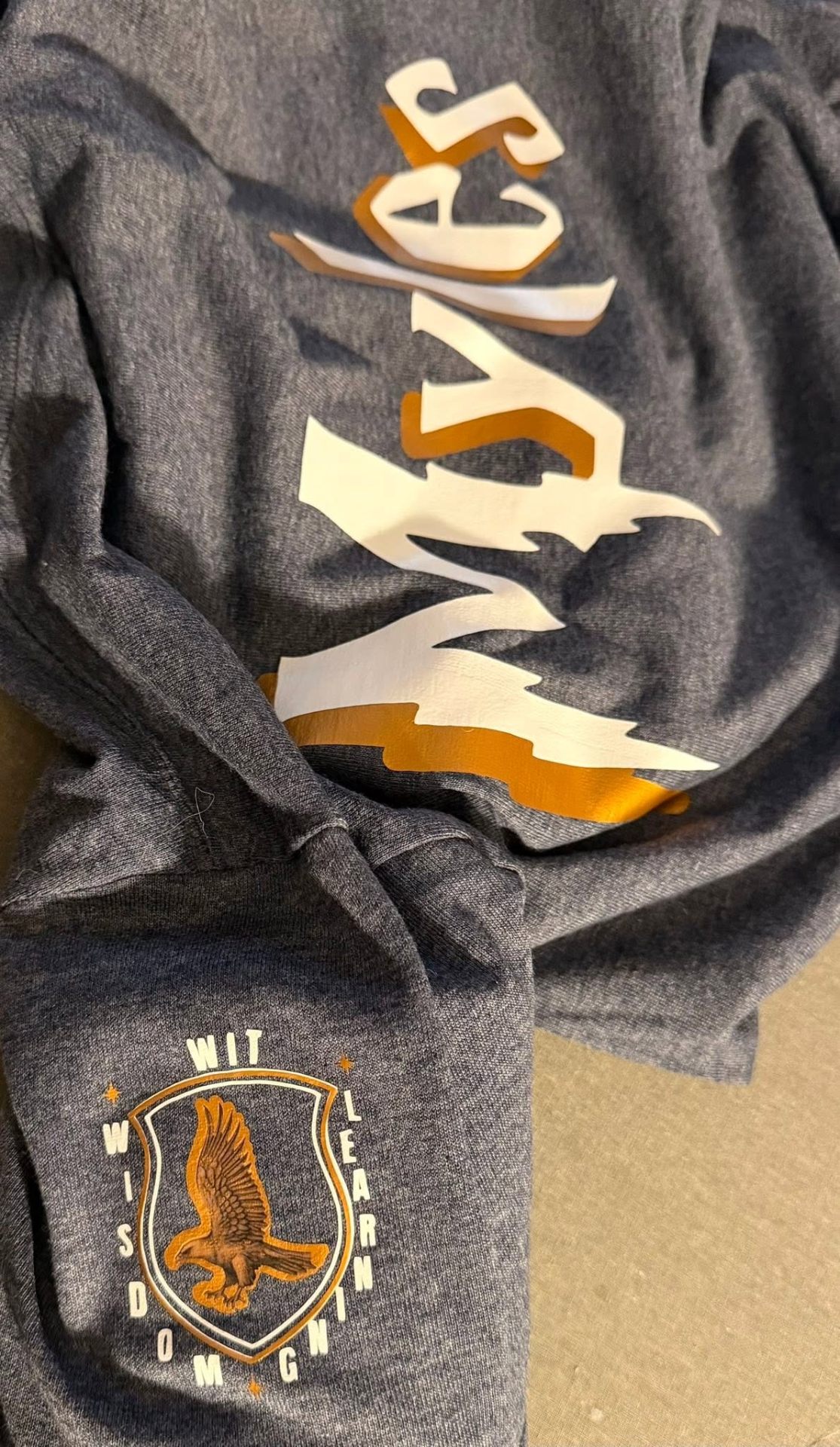 Close-up of the Myles lightning-bolt name tee with wisdom eagle sleeve emblem