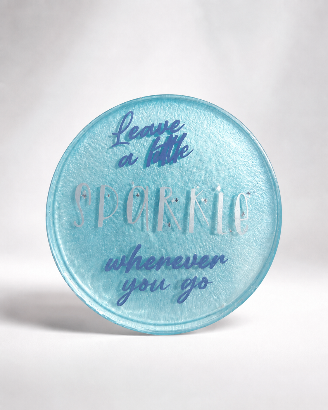 Aqua resin coaster with hand-lettered quote 'Leave a little sparkle wherever you go' in blue and silver