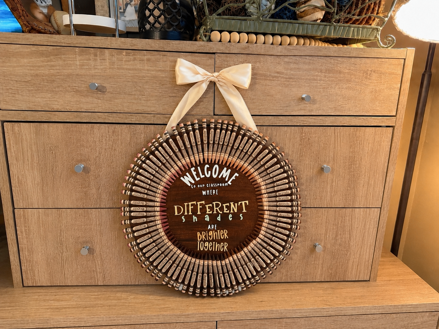 Handmade crayon wreath classroom door hanger with 'Welcome to our classroom where different shades are brighter together' quote and cream ribbon bow